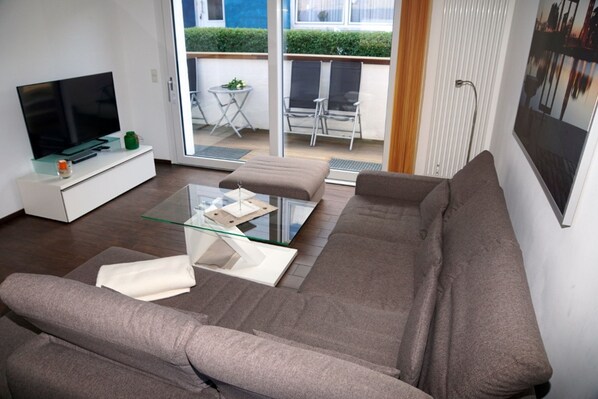 Una sala de estar moderna con un sofá, una mesa de centro de vidrio y un televisor de pantalla plana sobre un mueble blanco.