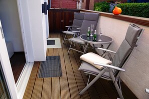 Una terraza de madera con una mesa, sillas, una parrilla pequeña y una planta en maceta.