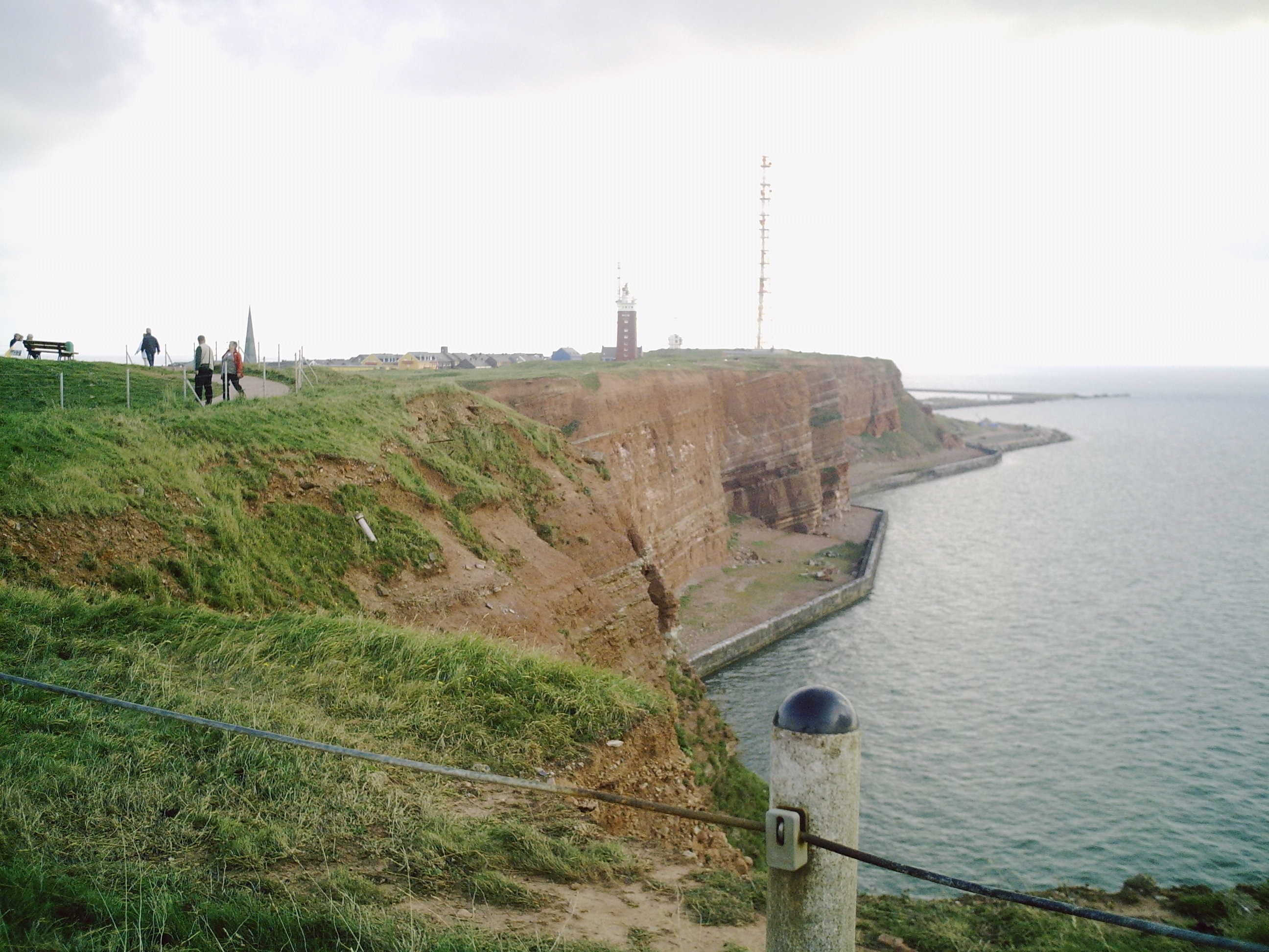 Une falaise côtière avec un phare, une zone herbeuse et un sentier pavé.