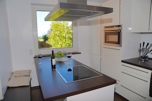 Una cocina moderna con una isla central, horno empotrado y ventana con vista a la vegetación.