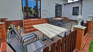 Une terrasse extérieure avec une table en bois et des chaises en métal, un mur en briques et une clôture en métal.