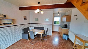 Une cuisine chaleureuse avec un coin repas, agrémentée d’un mur en briques, de poutres en bois au plafond et d’une petite fenêtre.