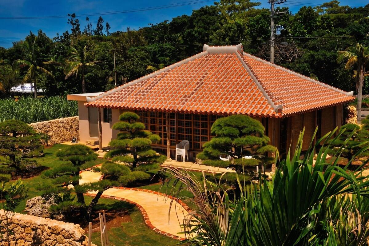 A traditional building with a tiled roof, surrounded by a landscaped garden with various trees and shrubs.