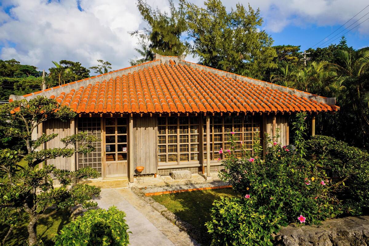 A traditional building with a tiled roof, wooden walls, and a garden with various plants and a small pond.
