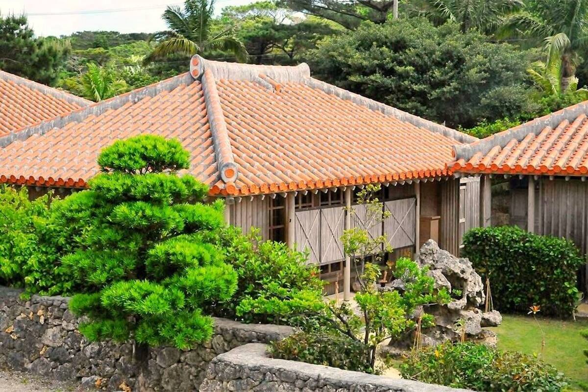 A traditional building with a tiled roof, surrounded by lush greenery and stone walls.