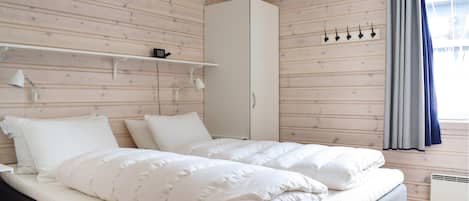 Un dormitorio con cama, armario, estante con lámpara y ventana con cortinas.