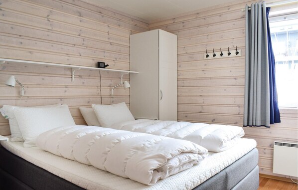Un dormitorio con cama, armario, estante con lámpara y ventana con cortinas.