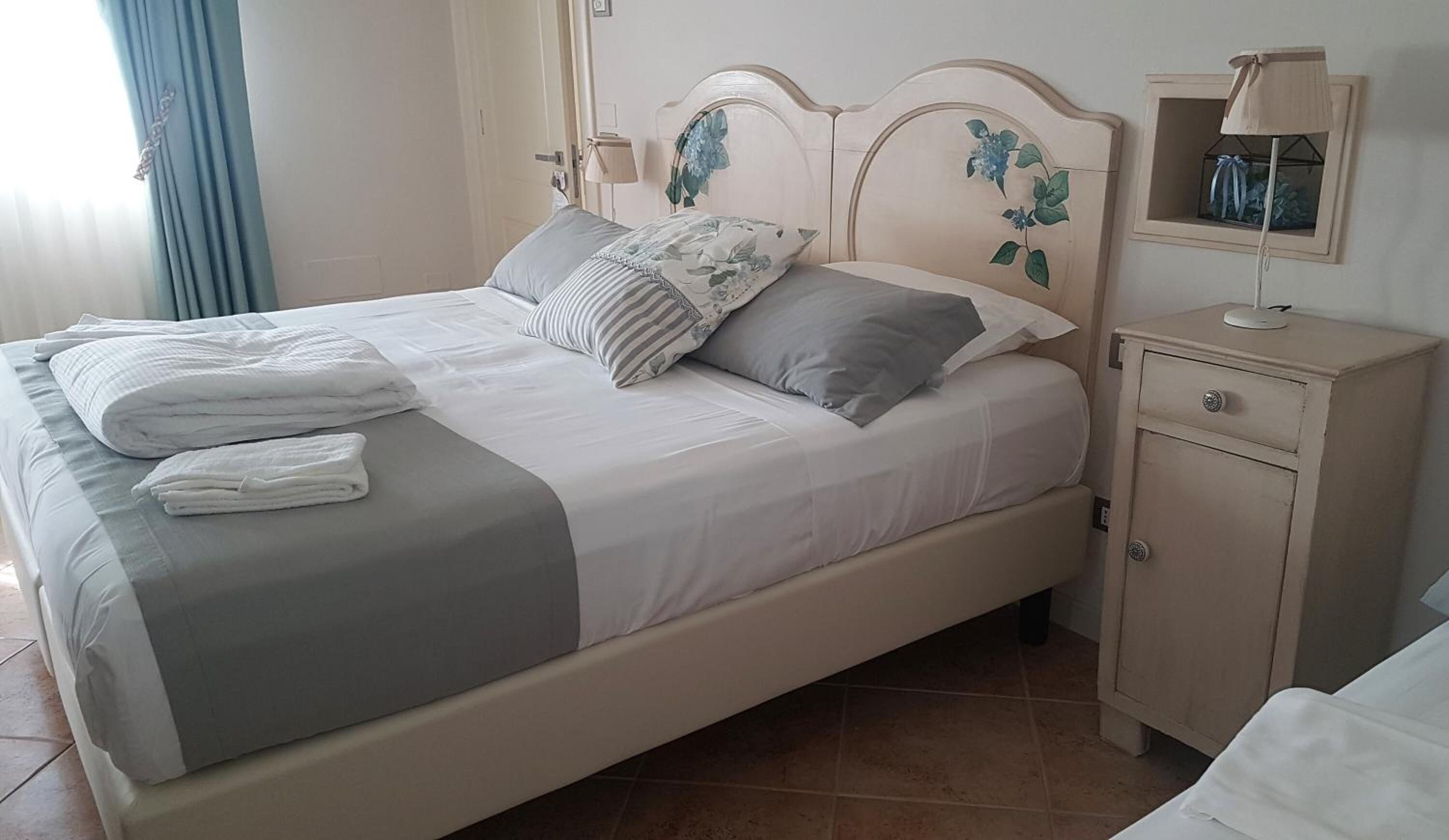 A neatly made bed with a grey and white bedspread, two pillows, and folded towels on the side.