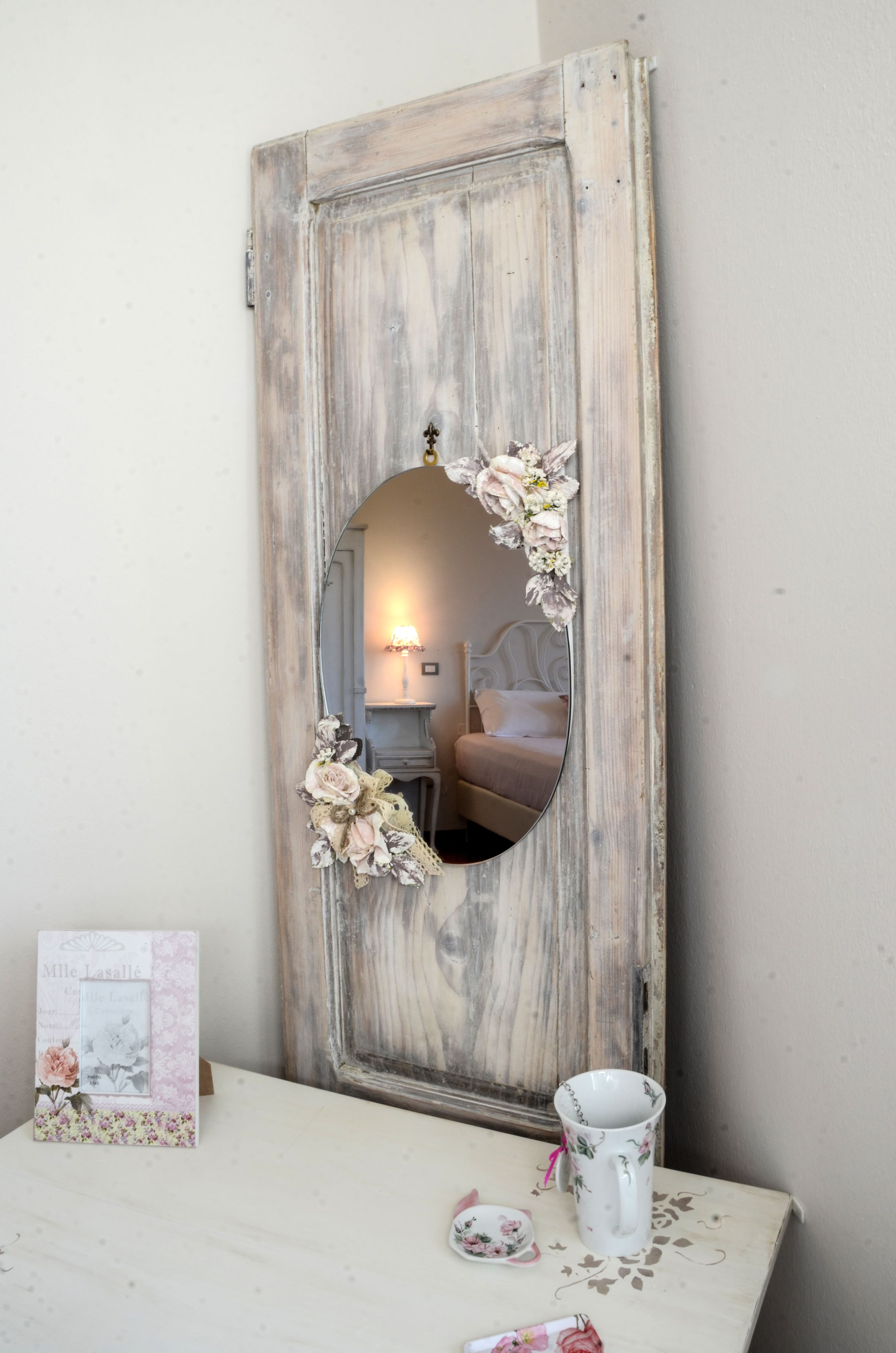 Un miroir rustique orné de motifs floraux, une petite table sur laquelle est posée une tasse à motifs floraux et une carte encadrée.