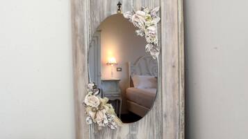 Un miroir rustique orné de motifs floraux, une petite table sur laquelle est posée une tasse à motifs floraux et une carte encadrée.