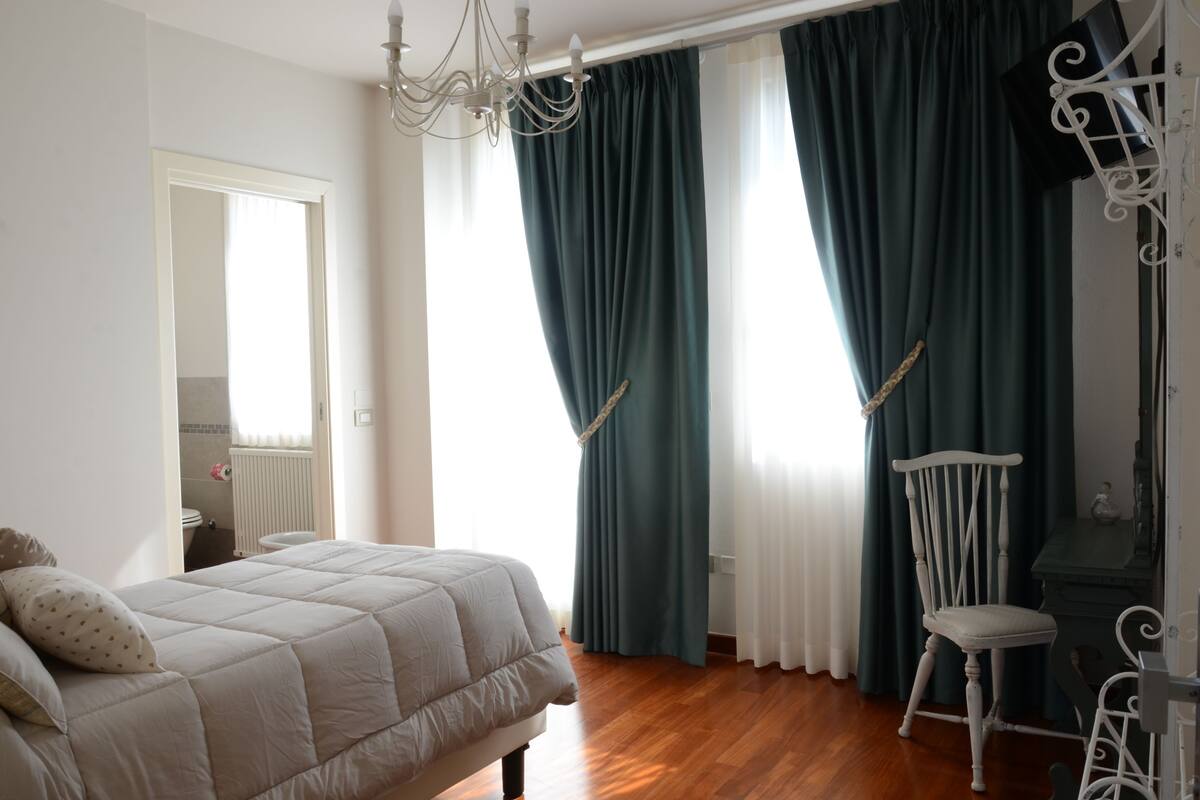 A bedroom with a bed, a chair, a dresser, and a window with curtains.