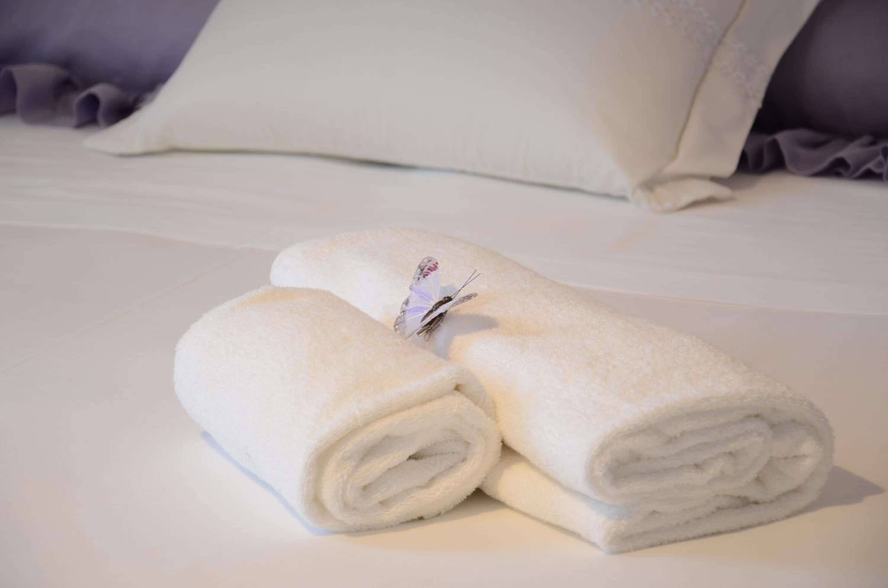 A neatly made bed with white linens and a rolled towel placed on top.