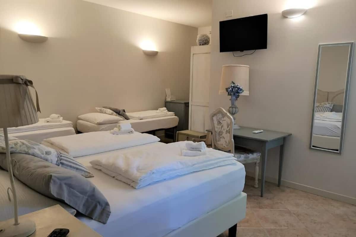 A hotel room with two beds, a desk, a chair, a TV, a mirror, and a lamp.