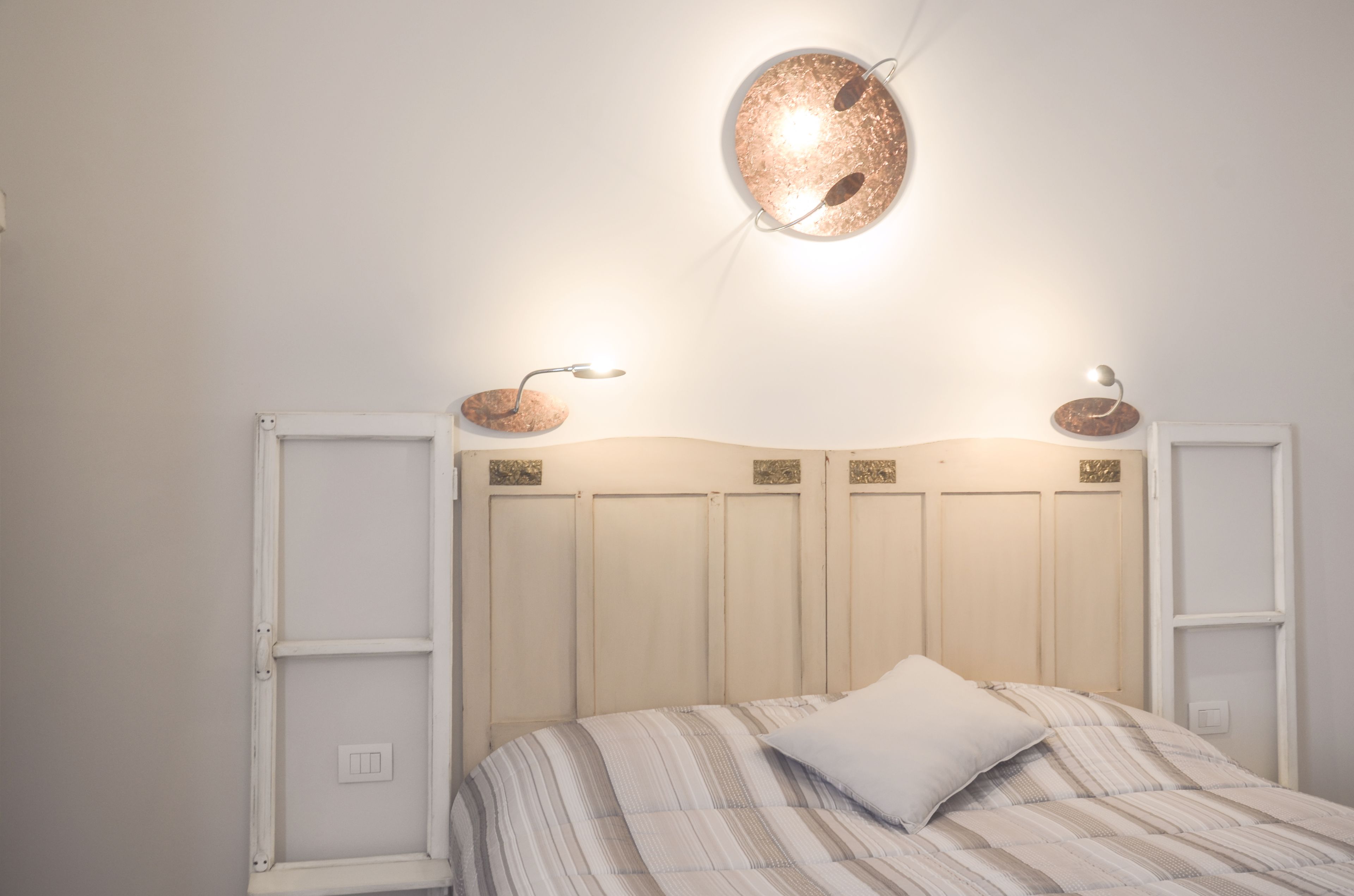 A bedroom with a bed, a headboard, and two wall-mounted light fixtures.
