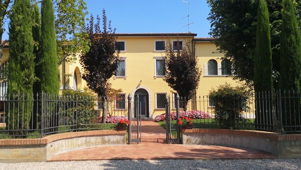 Un bâtiment jaune avec une entrée centrale, entouré d’une allée gravillonnée et d’une clôture en métal.