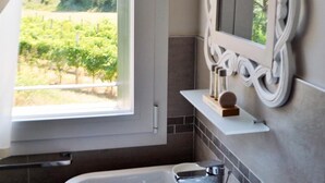 Une salle de bain avec un lavabo blanc, un miroir doté d’un cadre orné et une vue sur un vignoble par la fenêtre.