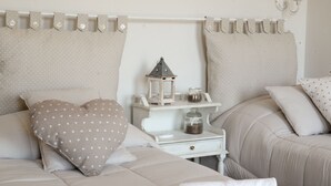 Un lit bien fait, agrémenté d’un coussin à motifs en forme de cœur, une petite table de chevet avec une lanterne et une commode blanche.