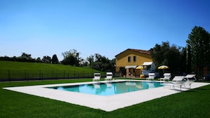 Une piscine rectangulaire bordée d’une terrasse blanche, entourée d’une pelouse bien entretenue. On y trouve des chaises longues et un parasol jaune près de la piscine.