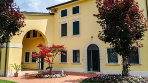 Un bâtiment jaune doté d’une arche centrale, de nombreuses fenêtres et d’un jardin bien entretenu où poussent des plantes à fleurs.