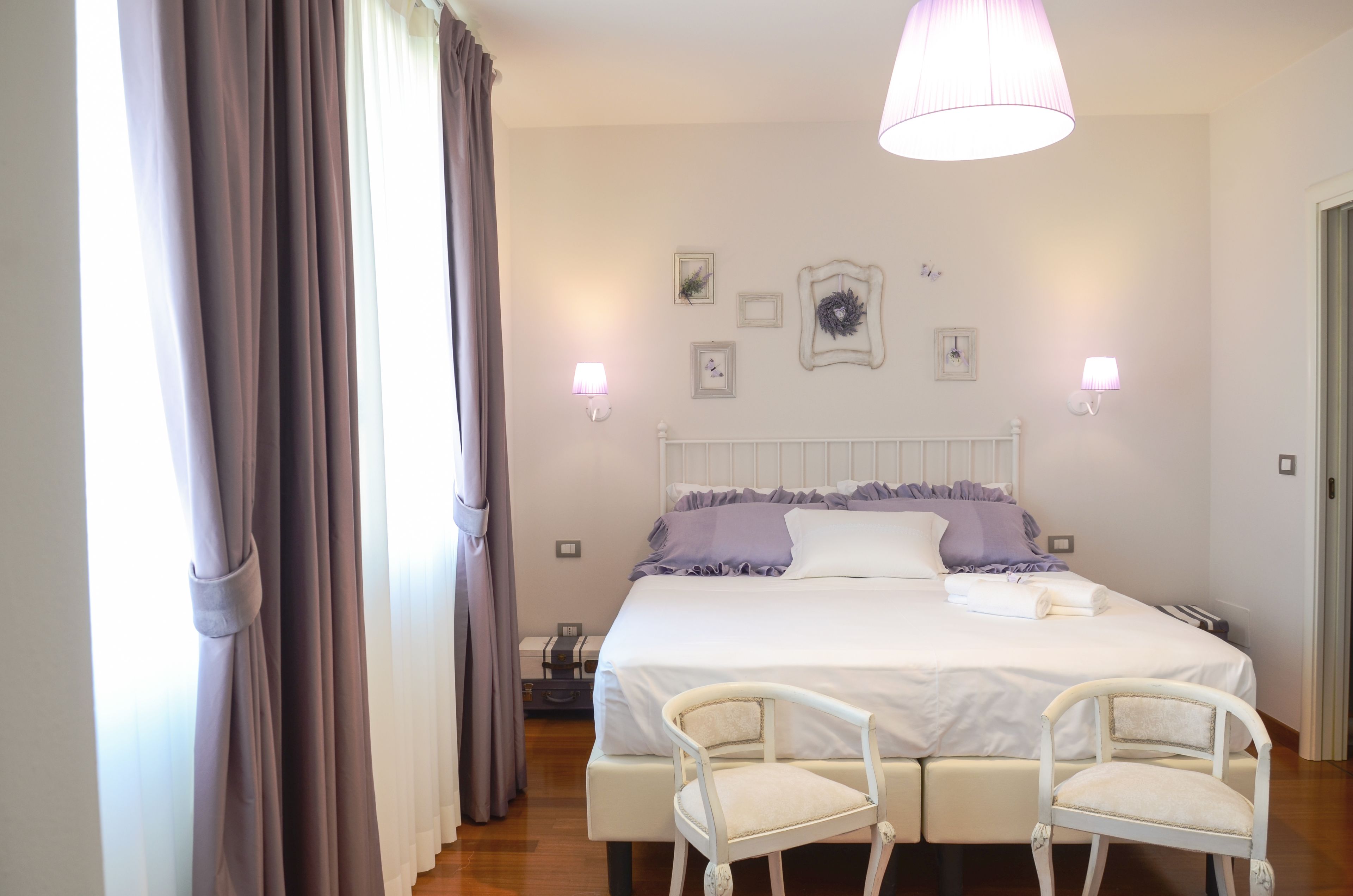 A bedroom with a large bed, two bedside tables, a white chair, and a hanging light fixture.