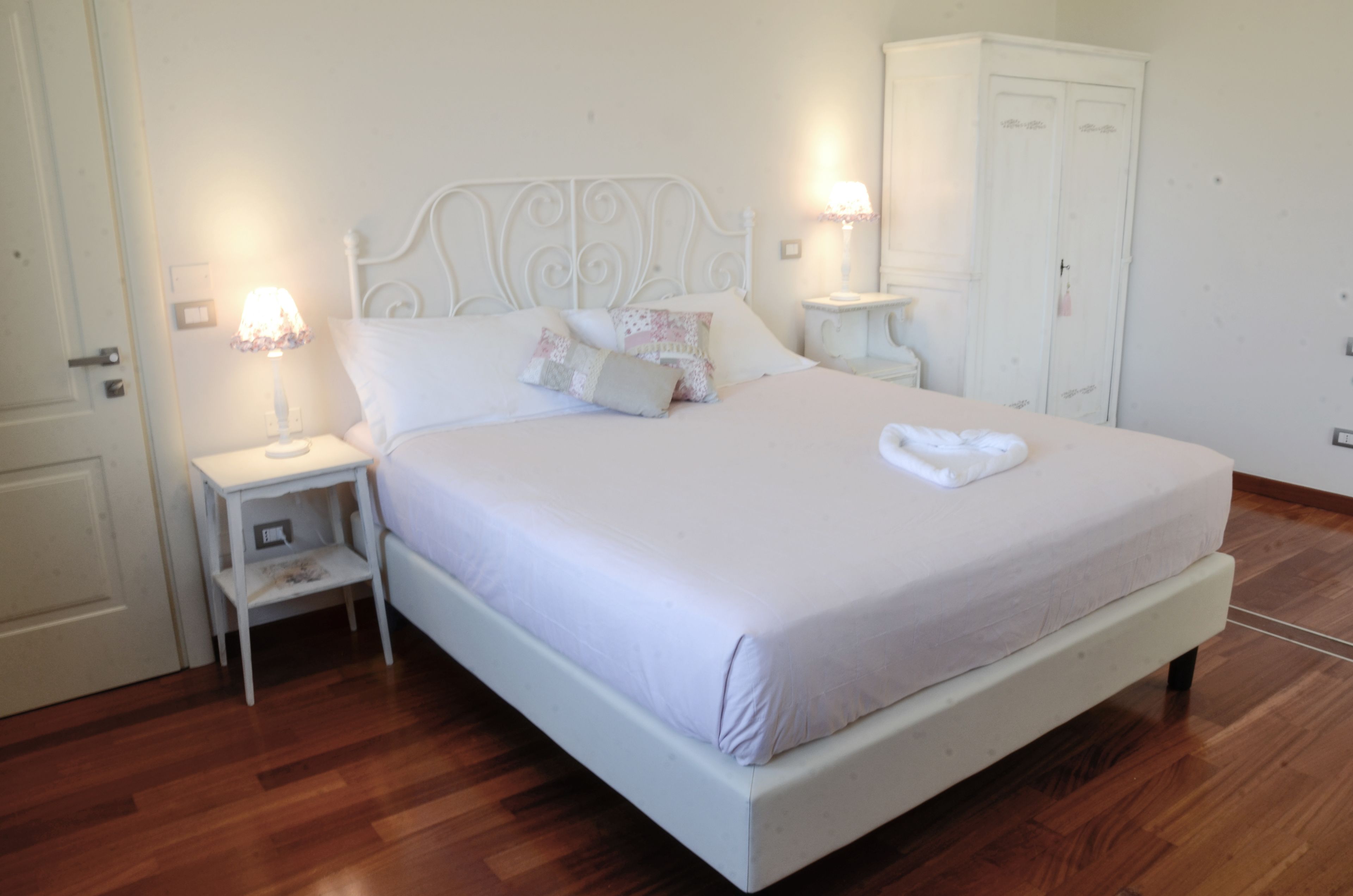 Um quarto com cama, mesas de cabeceira, guarda-roupa e uma porta.