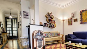 Un salon avec un sol à carreaux, un canapé bleu, une bibliothèque et un vieux juke-box.