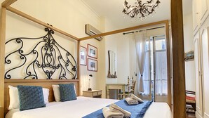Une chambre avec un grand lit, un lustre, un miroir et une vue sur l’extérieur.
