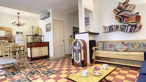 Un salon avec un sol à carreaux, un canapé, une table avec des tasses et une assiette, un juke-box et une bibliothèque.