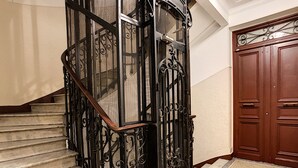 Un escalier orné de rampes en métal et d’une main courante en bois, menant à une porte surmontée d’une grille décorative en métal.