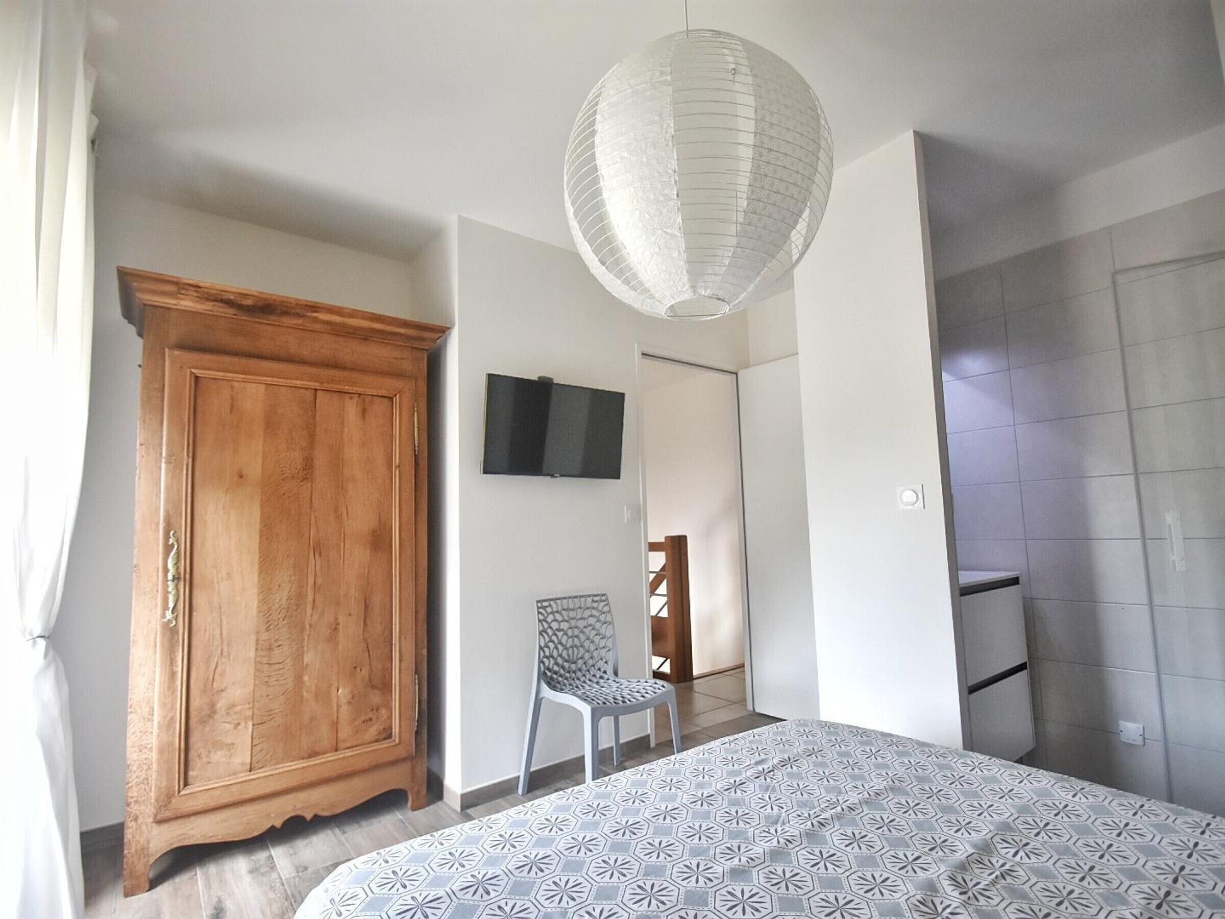 Una camera da letto con un letto, un'armadio in legno, una sedia, un televisore e una porta che dà su un'altra stanza.