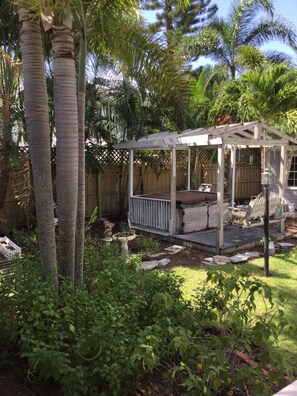 Relax in a serene, shaded patio surrounded by lush greenery and a birdbath.