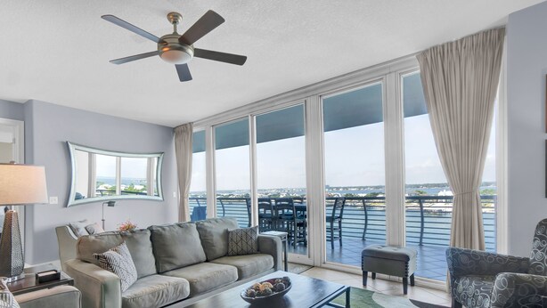 Ein modernes Wohnzimmer mit einer Couch, Sesseln, einem Couchtisch und einem Deckenventilator. Große Fenster bieten Blick auf das Wasser und die Skyline der Stadt.