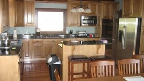 Une cuisine avec des meubles de rangement en bois, un réfrigérateur en acier inoxydable, un four à micro-ondes et une cuisinière. On y trouve également une poubelle et une table à manger avec des chaises.