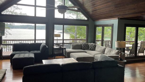 Un salon spacieux doté d’une grande fenêtre donnant sur un lac, d’un ventilateur de plafond et d’un coin salon confortable.