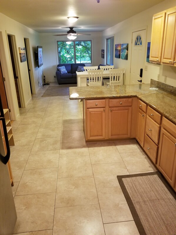 A kitchen with wooden cabinets, a granite countertop, and a dining area with a table and chairs. - Hawaiian plantation-style home, perfect for families. (Hauula)