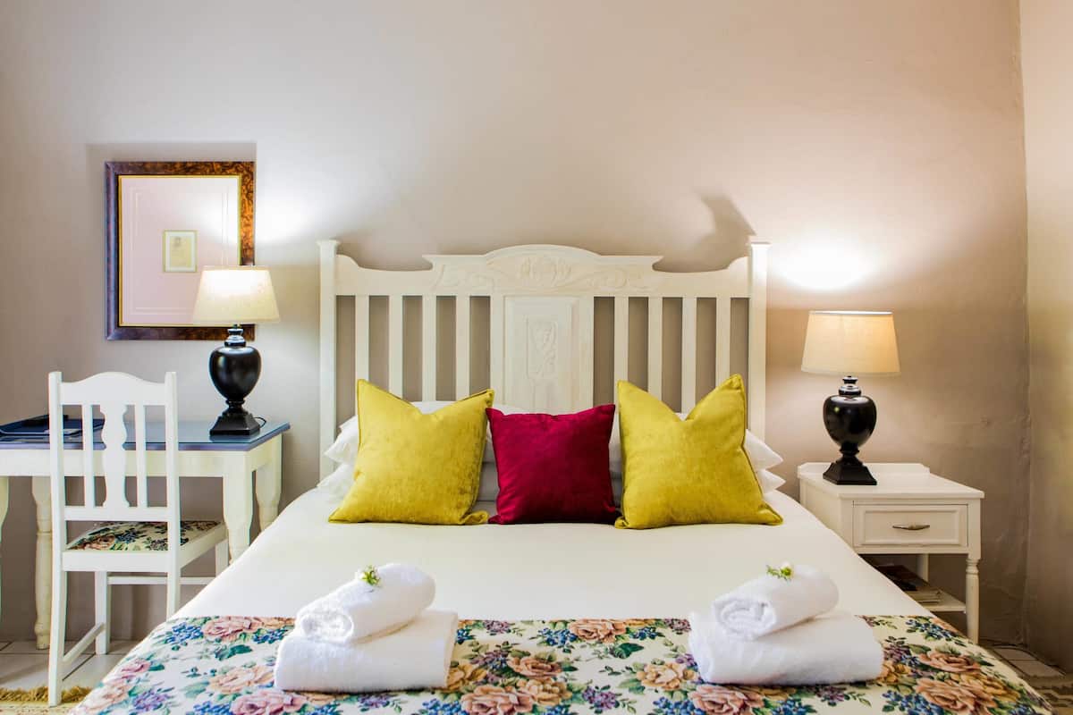 Una cama bien hecha con ropa de cama floral, cabecera blanca y dos lámparas de noche.