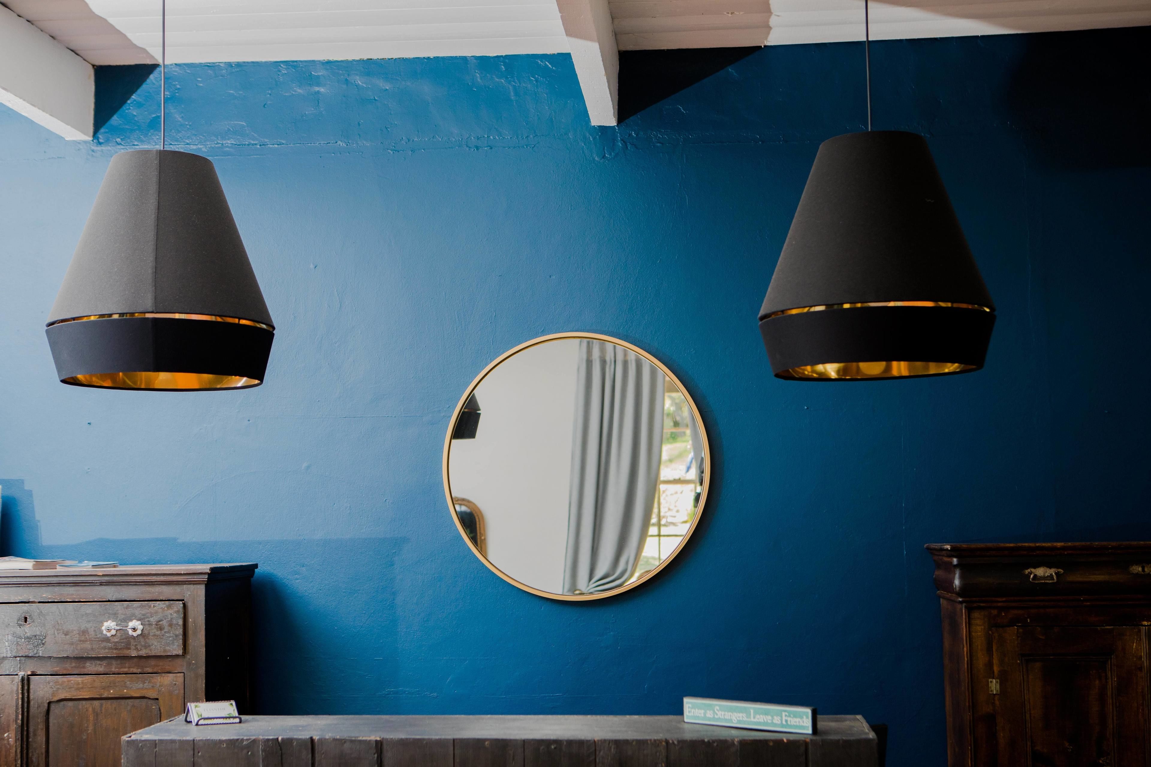 A room with a blue wall, a round mirror, and two hanging black lamps.
