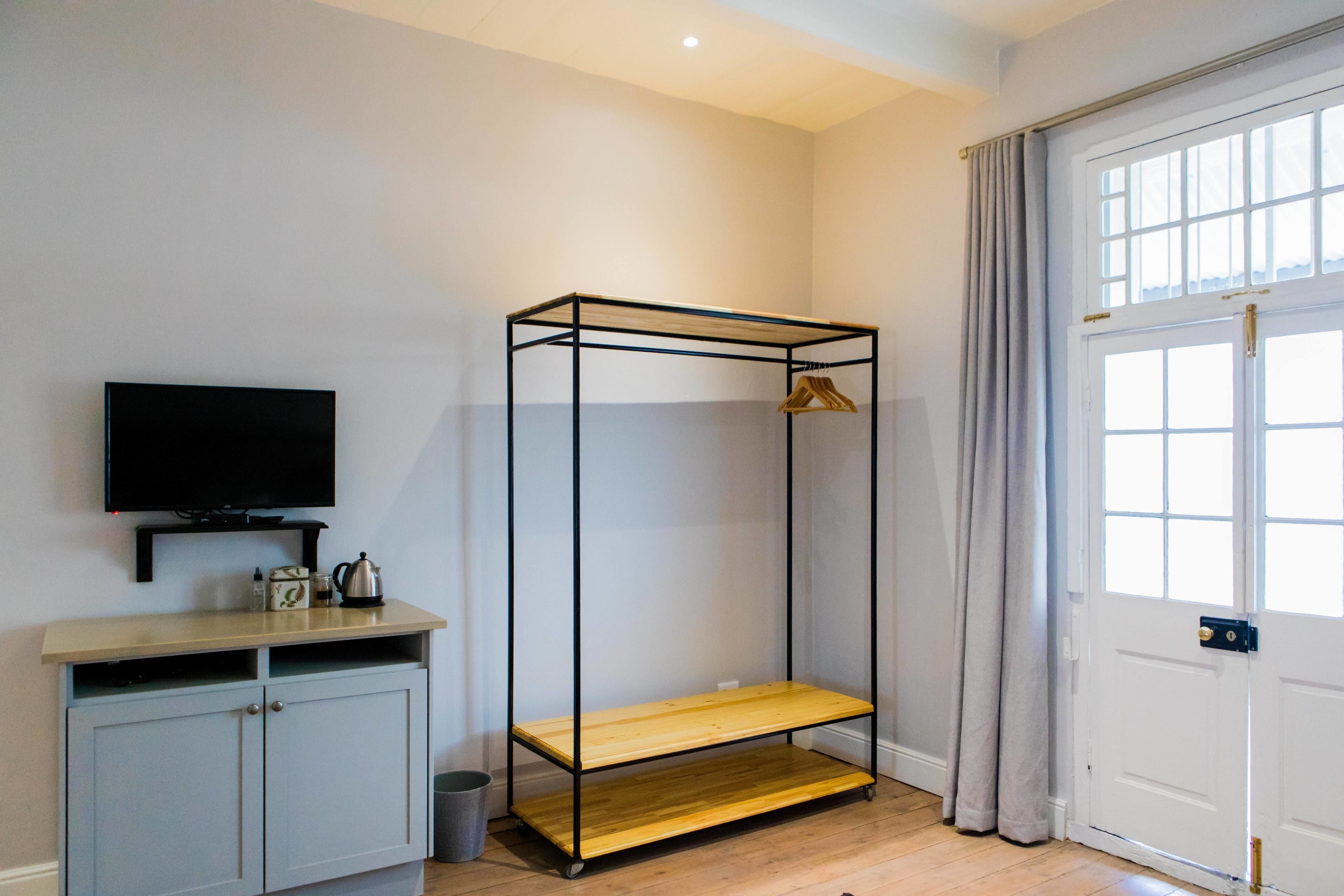 A room with a TV on a shelf, a wardrobe, a metal bed frame, and a door with curtains.