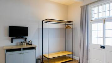 A room with a TV on a shelf, a wardrobe, a metal bed frame, and a door with curtains.