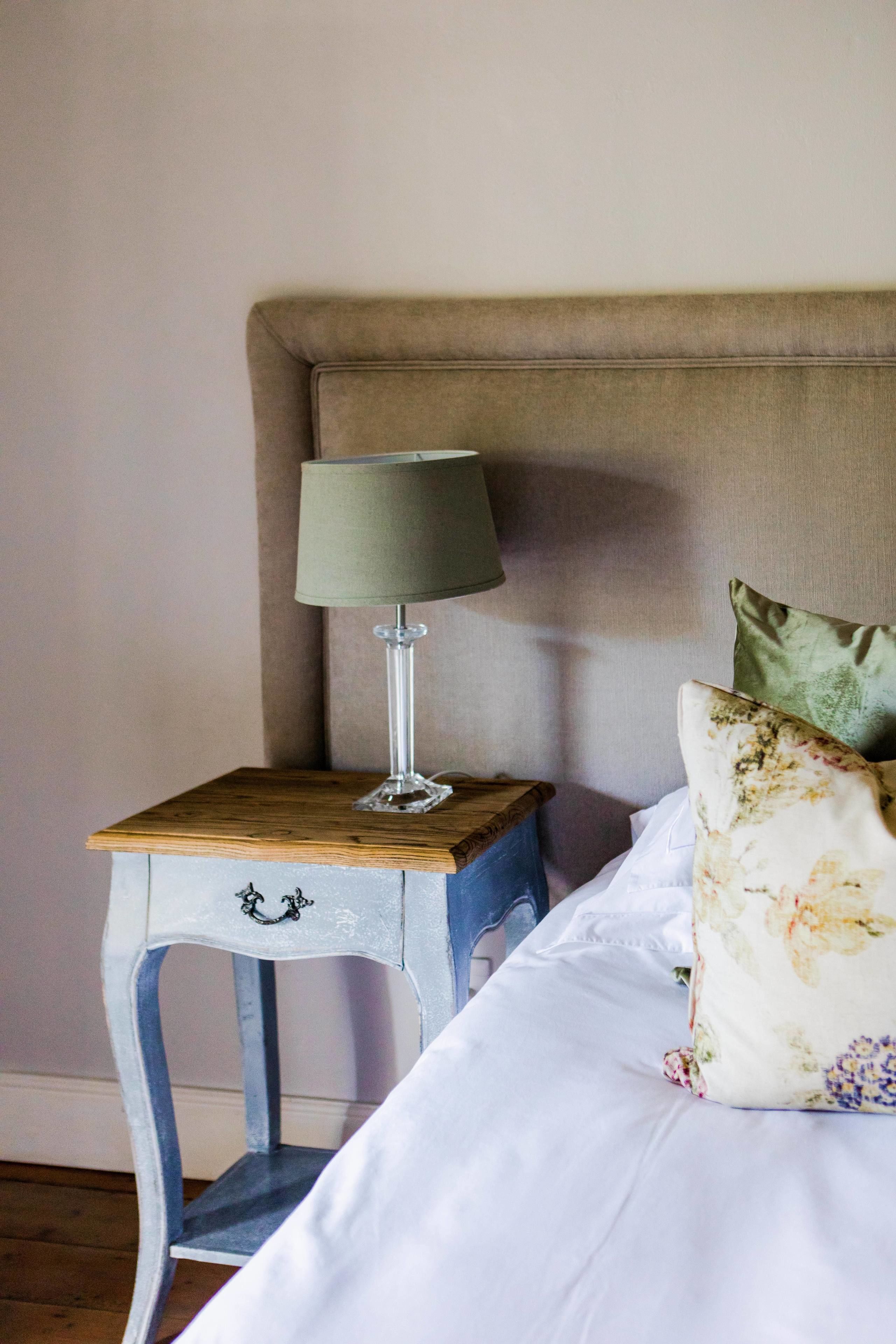 Un letto rifatto con cura, un cuscino a motivi floreali, una lampada da comodino su un comodino in legno e un piccolo oggetto decorativo sul comodino.