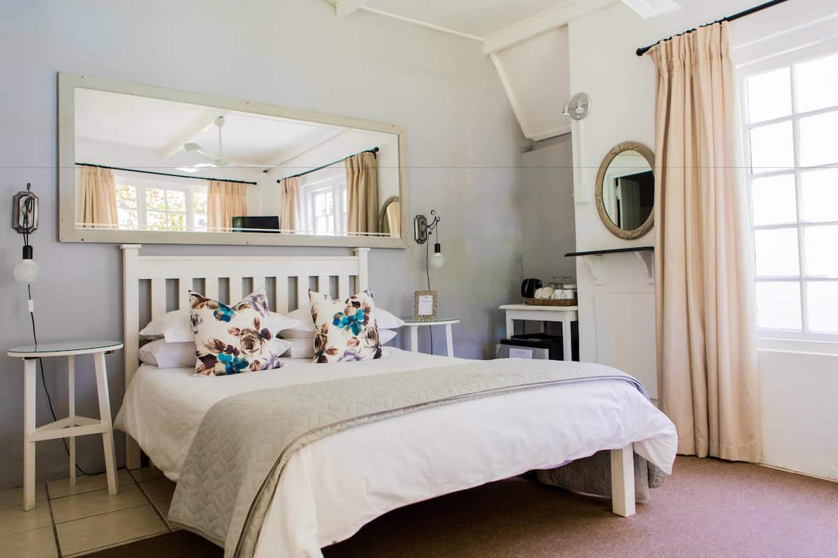 Un dormitorio con cama, un espejo grande, una mesita de noche, un aparador y una ventana con cortinas.
