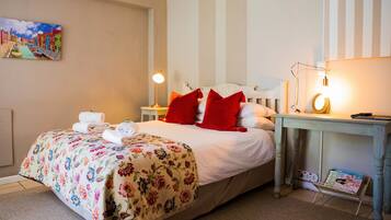 A neatly made bed with floral bedding, a bedside table with a lamp, and a wall-mounted painting.