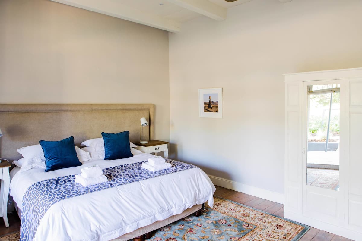 Un dormitorio ordenado con una cama grande, dos almohadas, una mesita de noche y una puerta que da al exterior.
