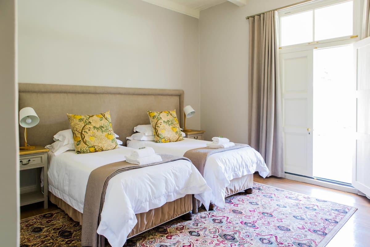 Habitación de hotel con dos camas, un tapete estampado y un amplio ventanal con cortinas.