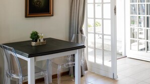 Un coin repas comprenant une table, des chaises, un tableau encadré et une vue à travers une porte vitrée.