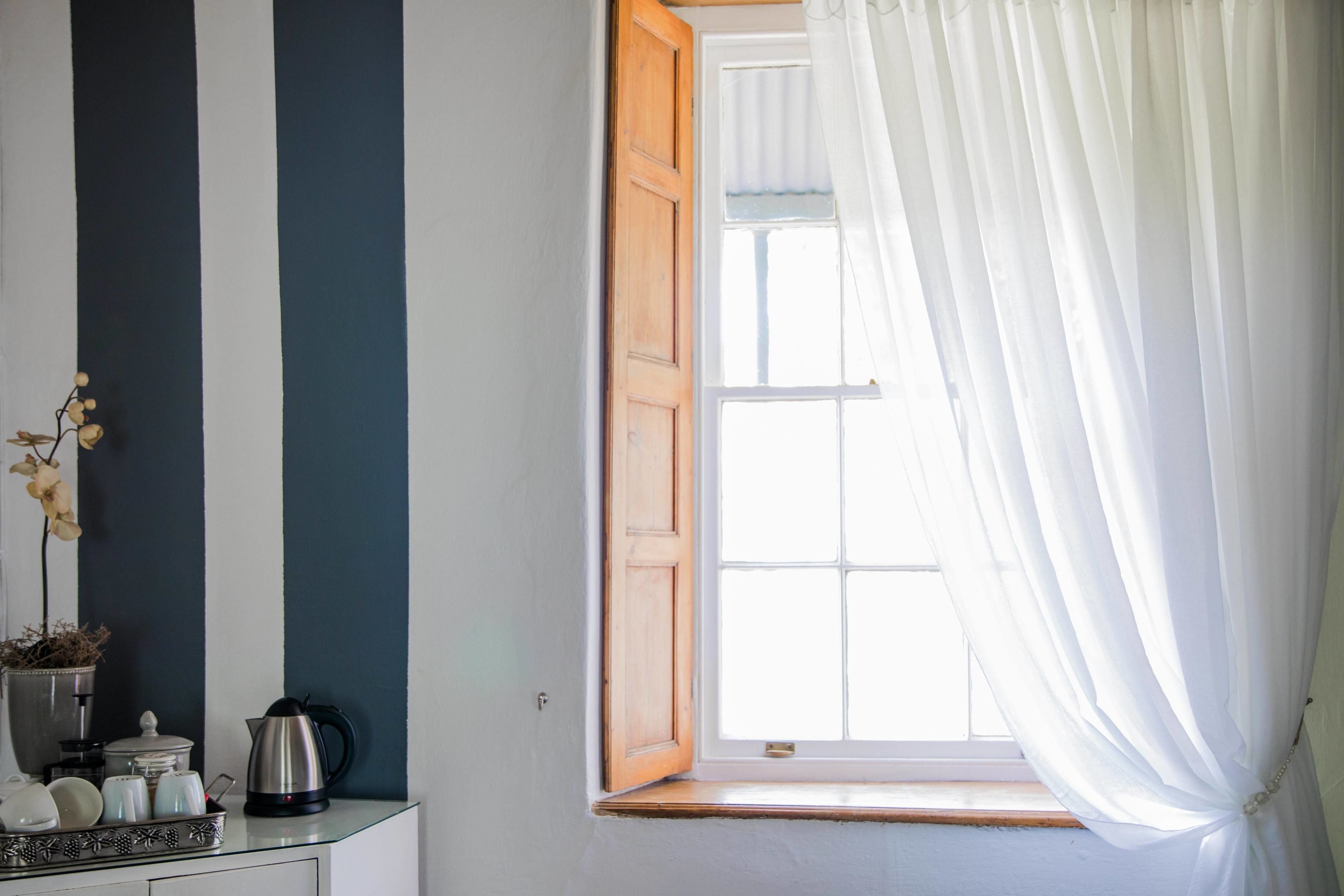 A room with a window, a wooden door, a white curtain, and a small table with a kettle and teapot.