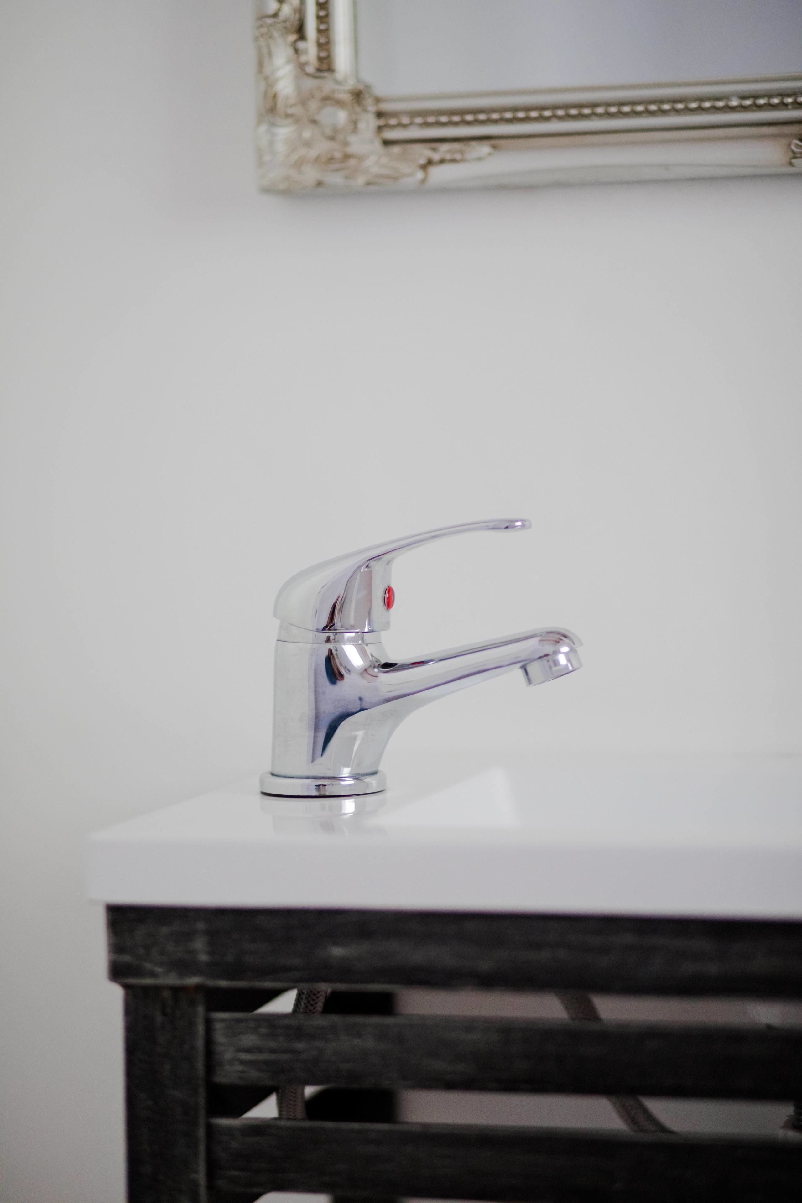 A bathroom with a chrome faucet on a white sink and a wooden stool.