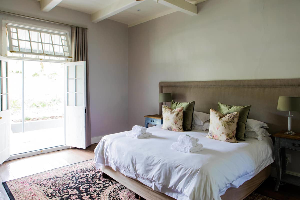 Un dormitorio con una cama grande, una mesita de noche, una lámpara y una ventana con cortinas.