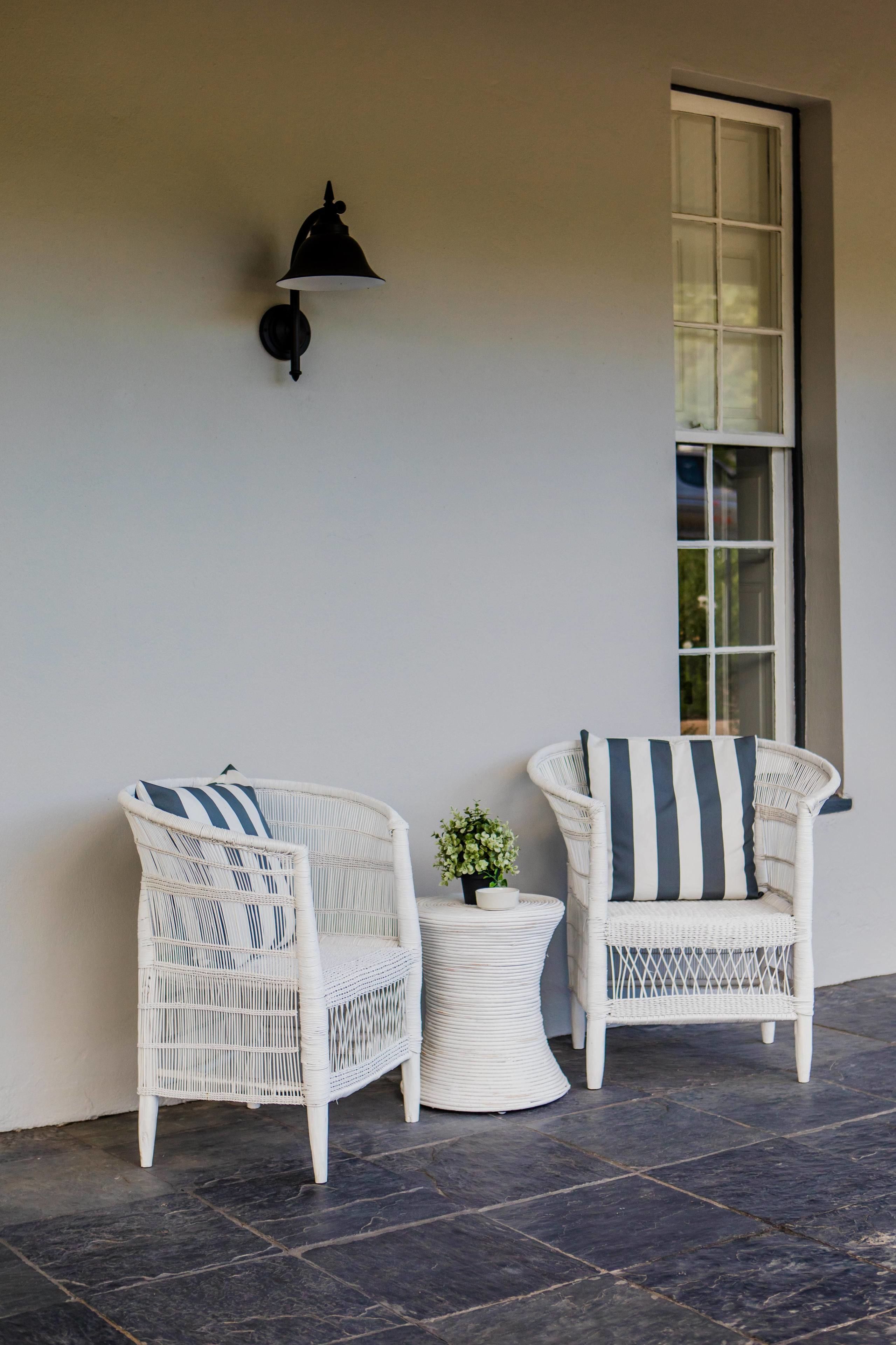 Two wicker chairs with striped cushions, a small round table with a plant, and a wall-mounted light fixture.