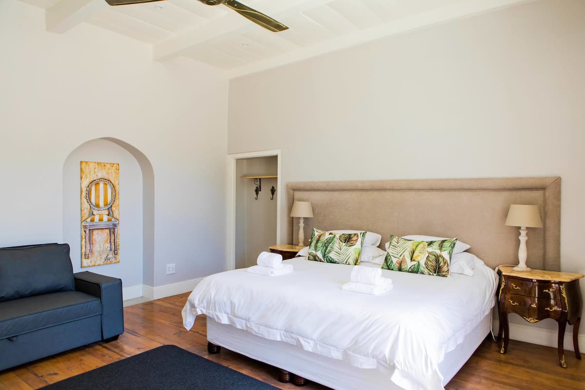 Habitación de hotel con una cama grande, un sofá, una mesita de noche y un cuadro en la pared.